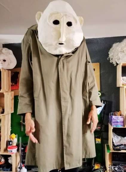 Persona que lleva una gran máscara blanca y una gabardina; en el interior.